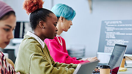 What the Gen Z? Zwei junge Menschen sitzen an ihrem Arbeitsplatz im Büro vor dem Laptop und arbeiten konzentriert.