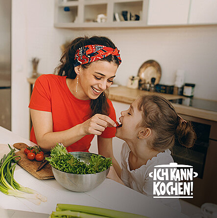 Mutter und Tochter naschen während des Kochens in der Küche eine Tomate