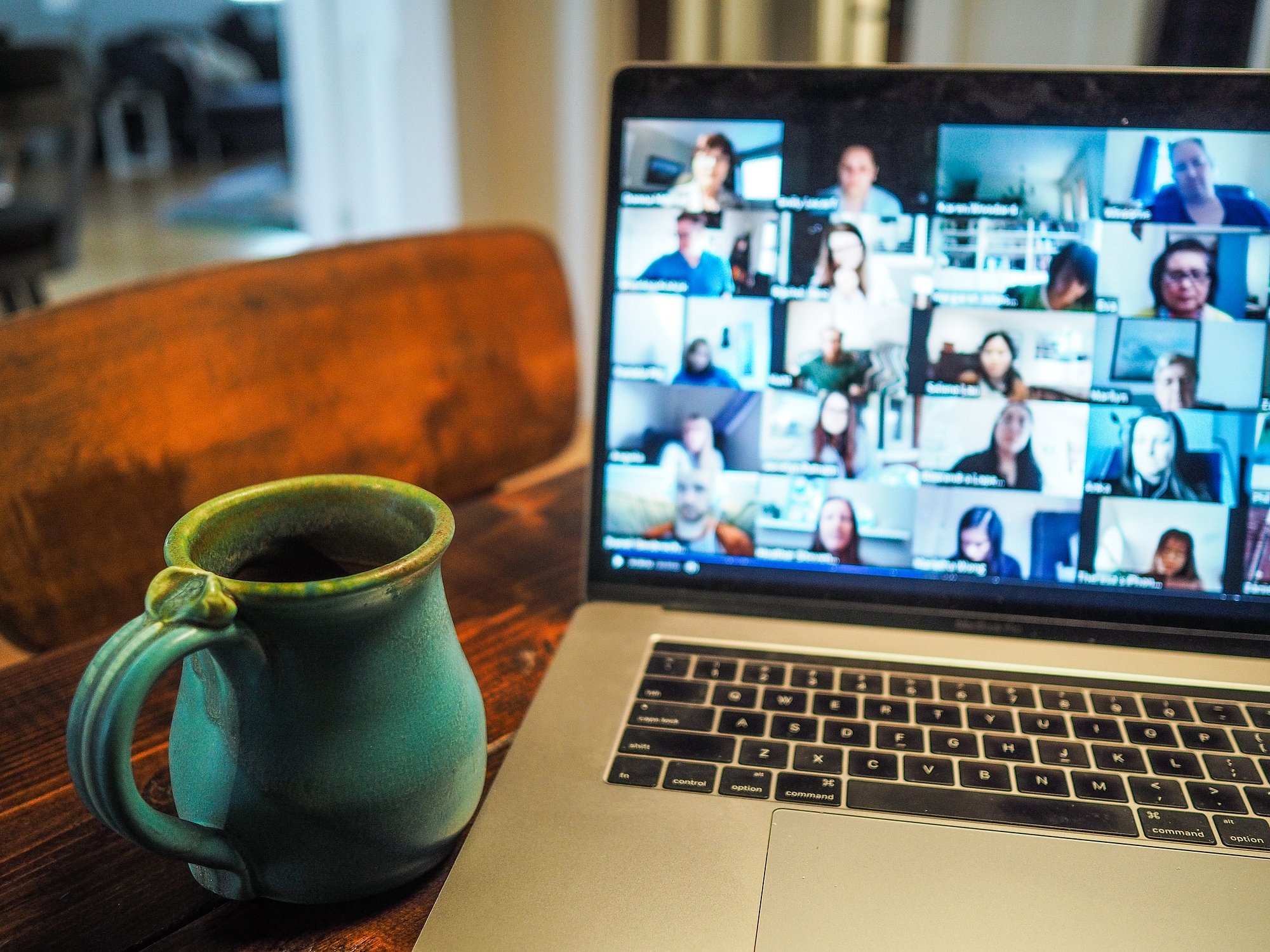 A laptop is on the table with a coffee in front of it and the screen shows that an online meeting is taking place.