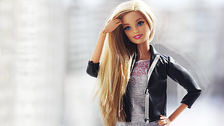 Box Office Barbie Blog A photo of Barbie with long hair and a leather jacket. She strokes her hair.