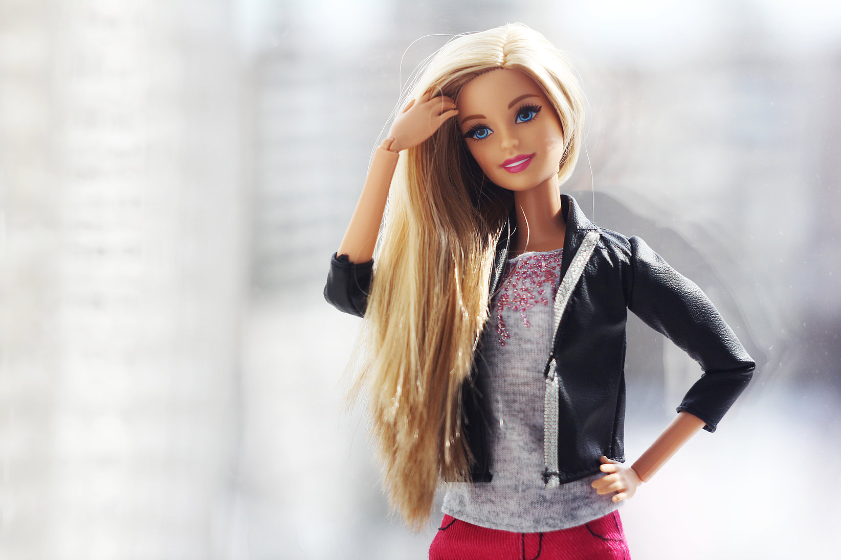 A photo of Barbie with long hair and a leather jacket. She strokes her hair.