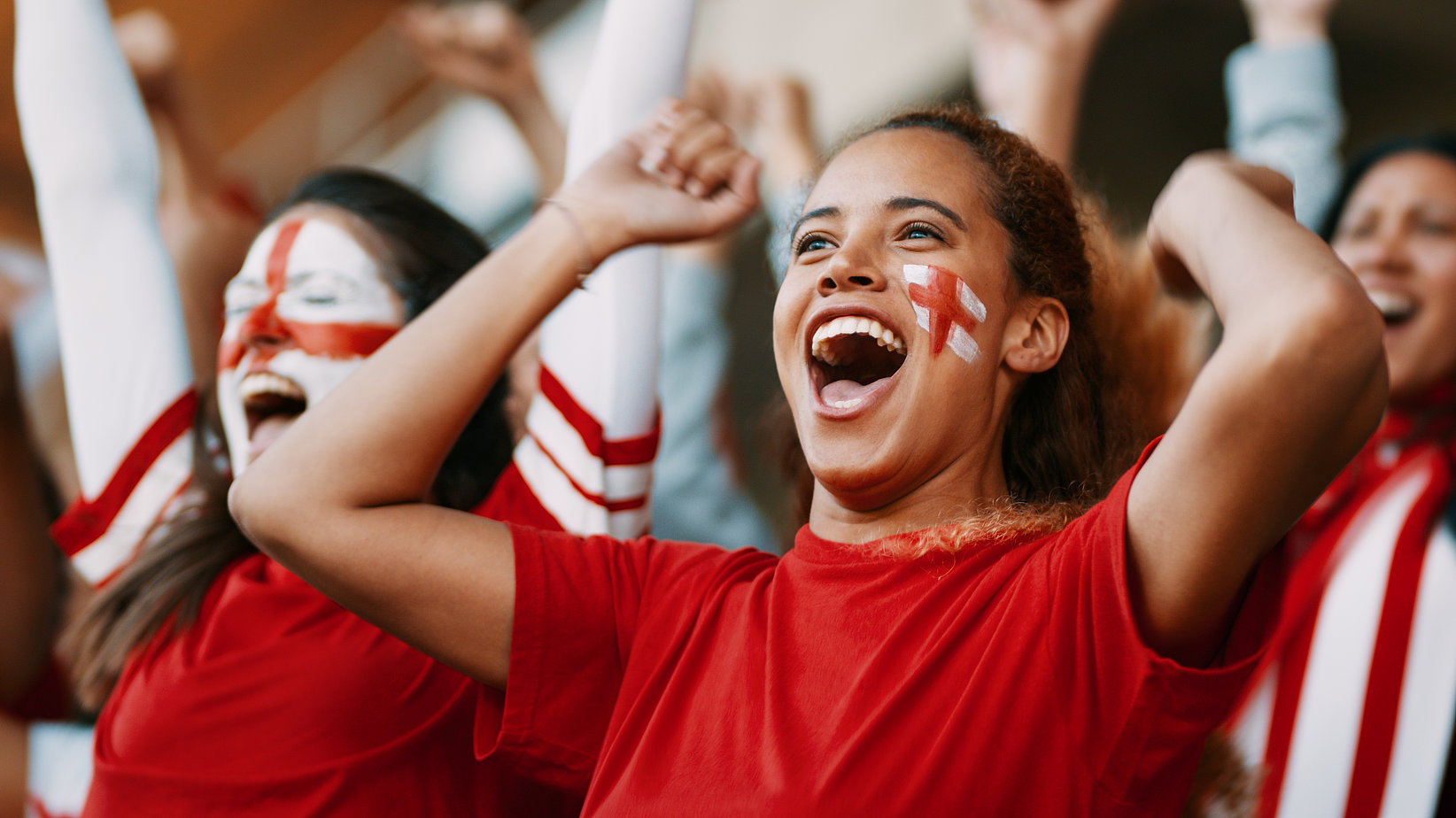 A woman has painted the England flag on your face and is wearing a red T-shirt. She is cheering and happy. 