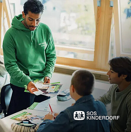 Lehrer erklärt zwei Schülern etwas im Klassenzimmer.