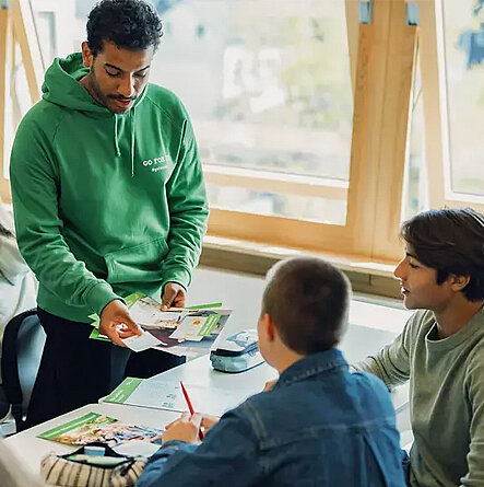 Lehrer erklärt zwei Schülern etwas im Klassenzimmer.