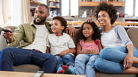 A Need For Consistency in Classification: BBFC Research Report A family with two children watches TV on the couch and smiles.