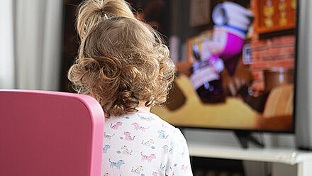 Mädchen sitzt auf einem Stuhl und sieht eine Spielzeugwerbung im Fernsehen.