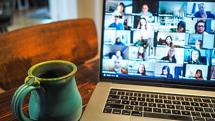 4 Tips for Running a Market Research Online Community A laptop is on the table with a coffee in front of it and the screen shows that an online meeting is taking place.