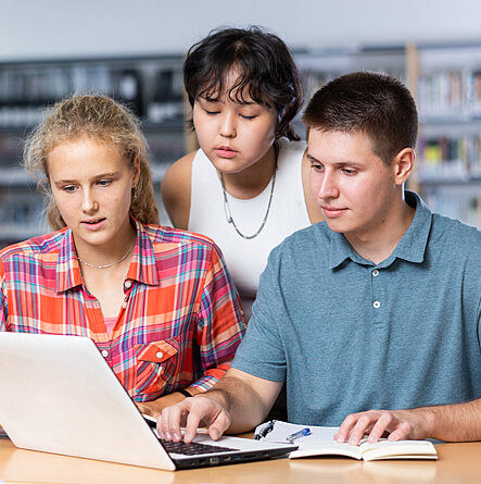 Gruppe von Schülerinnen und Schülern mit einem Laptop in der Bibliothek.