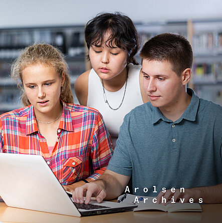Gruppe von Schülerinnen und Schülern mit einem Laptop in der Bibliothek.