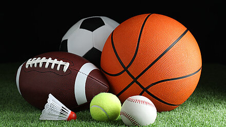 What's So Special About Sports Specialisation? Several sports balls and a shuttlecock lie on green artificial turf against a black background.