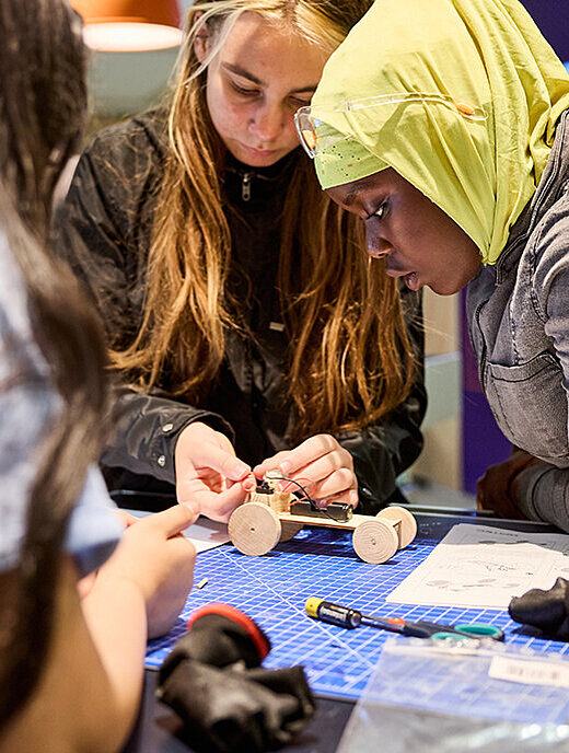 Mädchen tüfteln an einem Modellauto in vereinfachter Form aus Holz