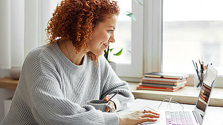 Lehrerin sitzt lächelnd an ihrem Arbeitsplatz vor einem Laptop.