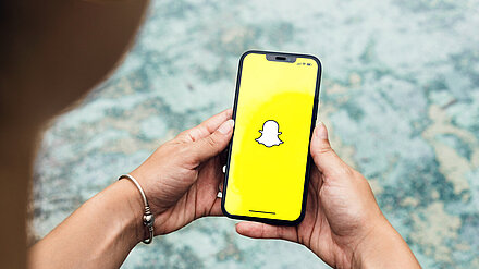 Snappy Safe Settings Person is holding a mobile phone and the Snapchat app can be seen on the screen.