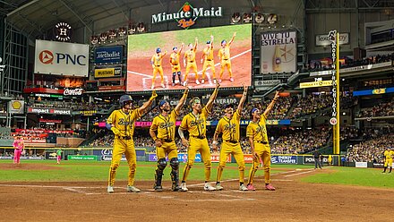 Banana Ball: The Future of Baseball, Sports Sacrilege or Just a Bit of Fun? Baseball players in yellow uniforms cheering on the field and pointing in the air while surrounded by a crowded stadium.