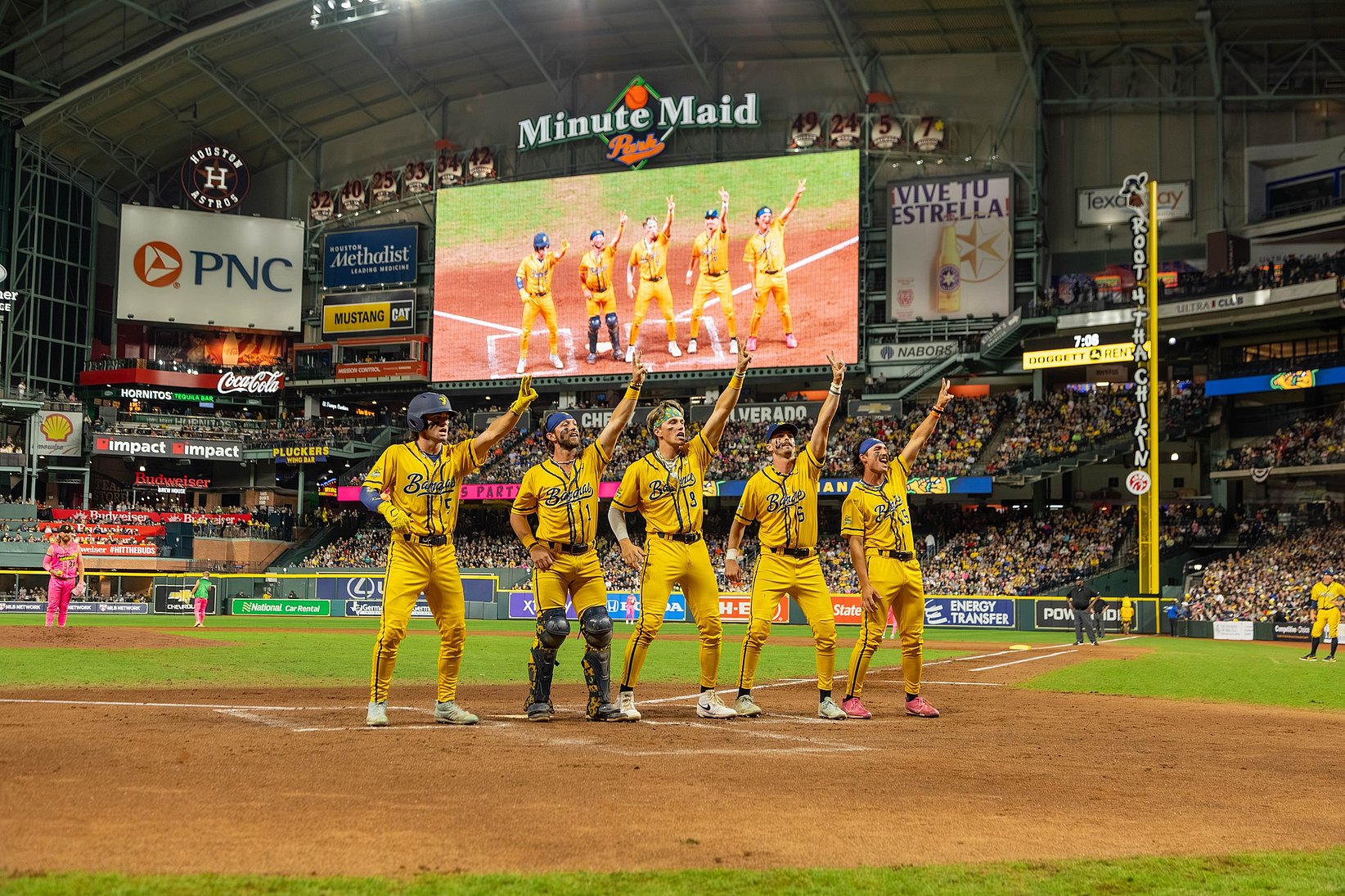 Baseball players in yellow uniforms cheering on the field and pointing in the air while surrounded by a crowded stadium.