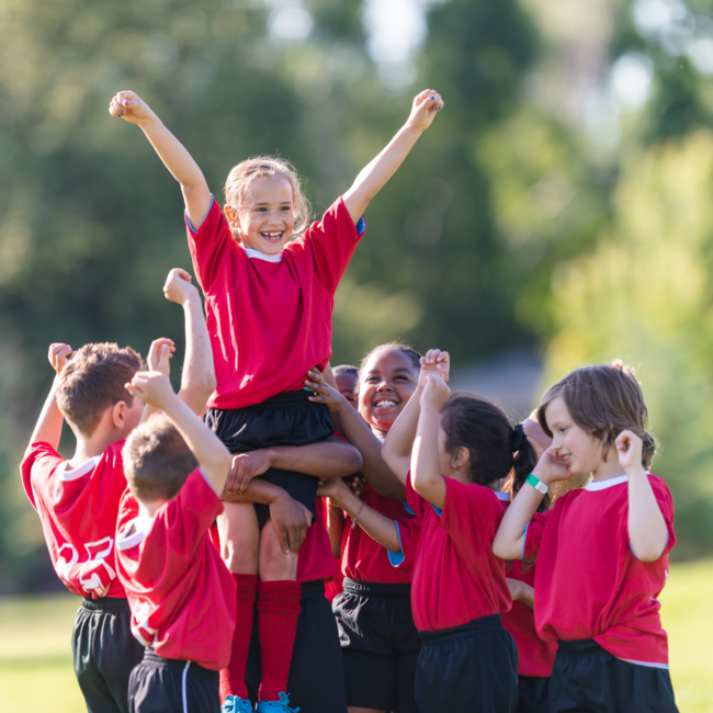 Soccer team of young children cheer and carry a girl from their team on their hands.