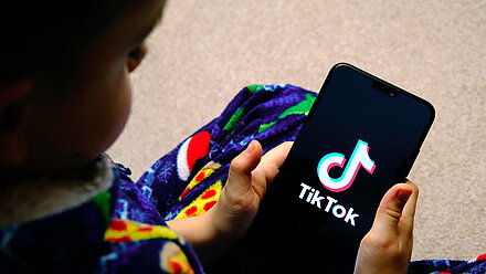 The Ukraine War’s Impact on TikTok Content Producers A mobile phone is held in the hand of a little boy, where "TikTok" can be seen on the screenshot.