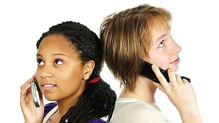 Are Teens Turning Away From Tech? Two teenagers (girl and boy) are standing back to back and talking on an old flip phone.