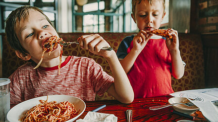 We are Family Research 2022 – Food And Me Two little boys are eating spaghetti and pizza at the table.