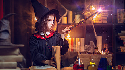 From Star Wars to The Beatles: Tweens’ Online Fandom Practices and What’s Next Child in a wizard costume pointing a wand at an open book in a magical setting. In the foreground are various colorful bottles and jars indicating alchemy or magic potions.