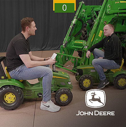 Zwei Männer auf grünen Kinder-Traktorspielfahrzeugen