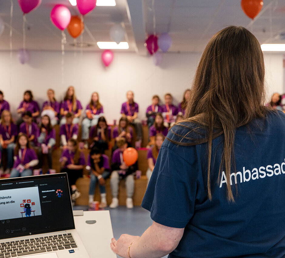 Frau steht in dunkelblauem Tshirt vor Gruppe Jugendlicher