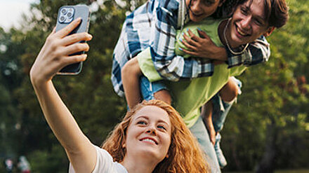 Drei Teenager sind auf einer Wiese und machen ein Selfie.