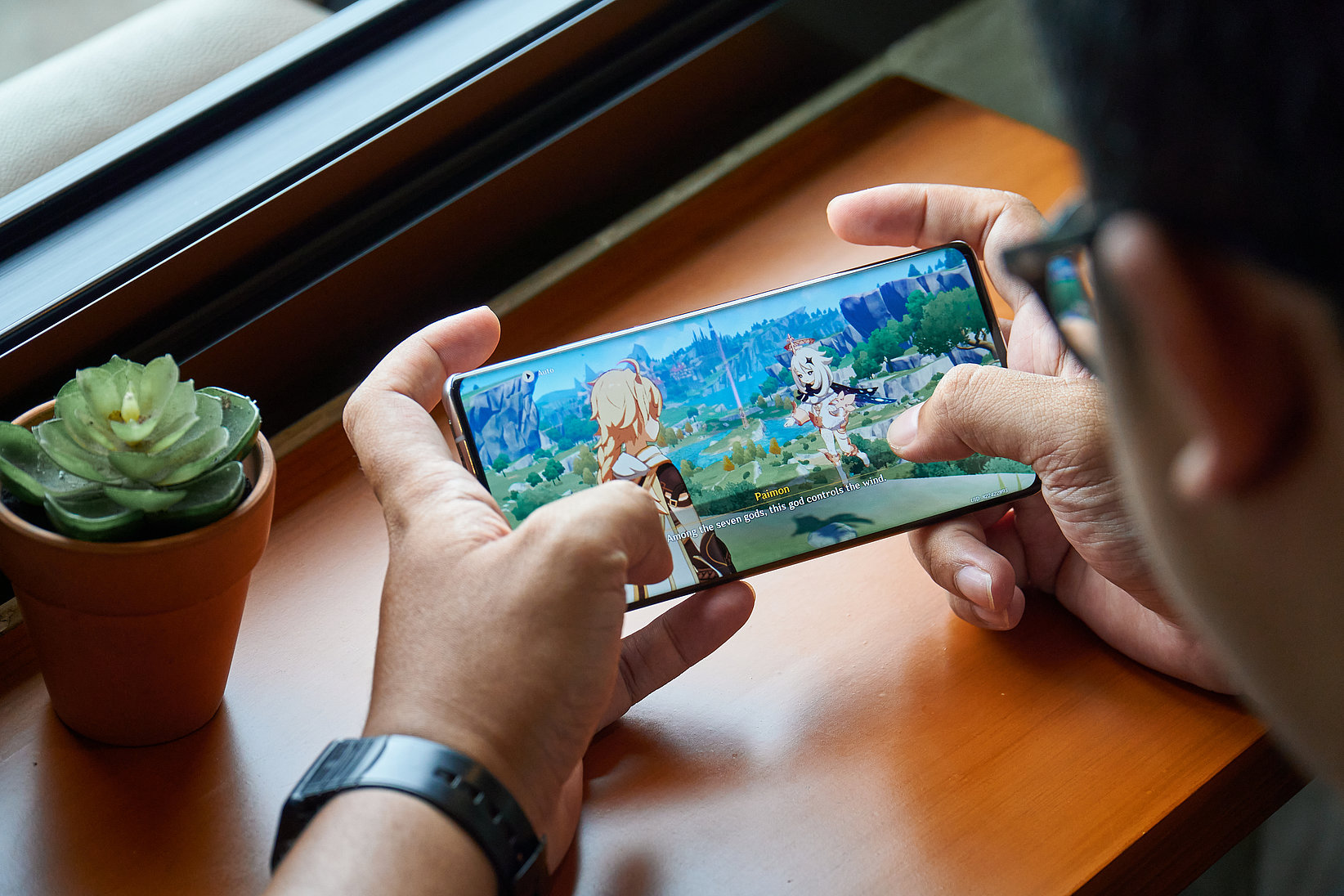 A mobile phone is held in the hand, where the screenshot shows that the fantasy action role-playing game "Genshi Impact" is being played.