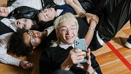 Generación Z al mando: cómo los jóvenes están transformando el marketing corporativo en TikTok Un grupo de jóvenes está acostado en el suelo, uno de ellos sonríe mientras mira su teléfono. Los amigos parecen relajados y unidos, compartiendo un momento juntos.