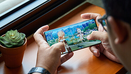 Genshin Impact: Have You Heard of It? A mobile phone is held in the hand, where the screenshot shows that the fantasy action role-playing game "Genshi Impact" is being played.