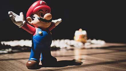 How Video Games Use Characters to Build Fandom A small Super Mario Bart figure, with his arms up, stands in the foreground of the picture and the background is dark.