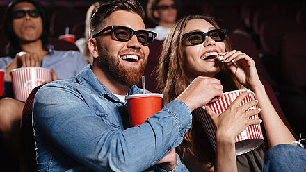 Is Smell-O-Vision making a comeback? A woman and a man sit smiling in a cinema, watching a movie with 3D glasses and eating popcorn.