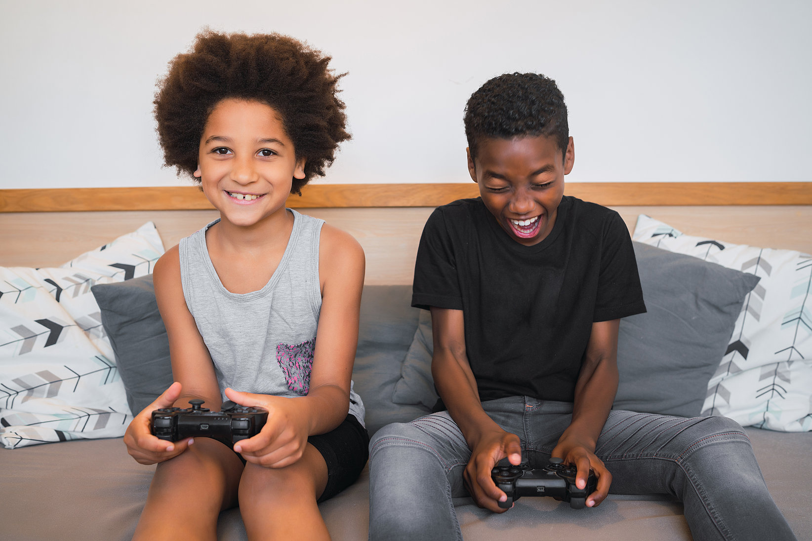 Two boys sit smiling on a sofa while they play a game.