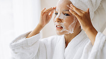 Vorsorge statt Nachsorge Mädchen steht im Bademantel vor dem Spiegel und macht eine Gesichtsmaske.