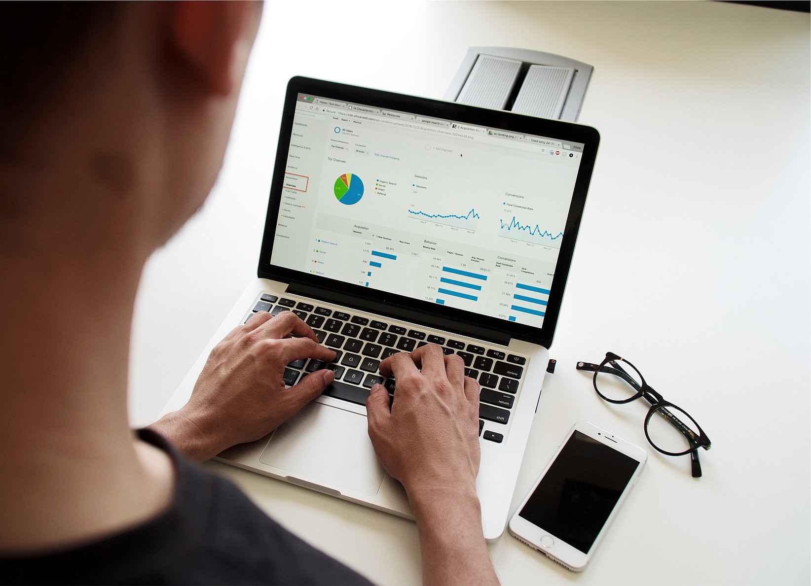 Person works on a laptop with a data analysis dashboard, with a pair of glasses and a smartphone on the desk next to it.