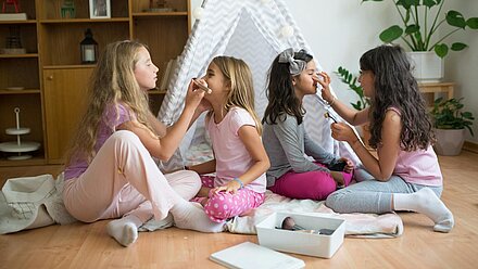 El fenómeno ‘Sephora Kids’ que afecta a la generación Alpha Cuatro niñas están jugando a maquillarse mutuamente en el suelo, frente a una tienda de campaña decorada. Parecen estar disfrutando de una pijamada en una habitación acogedora.