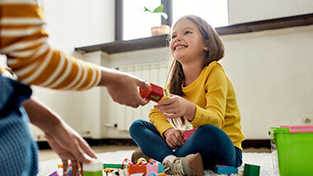 Mädchen sitzt auf dem Boden und spielt mit Bauklötzen