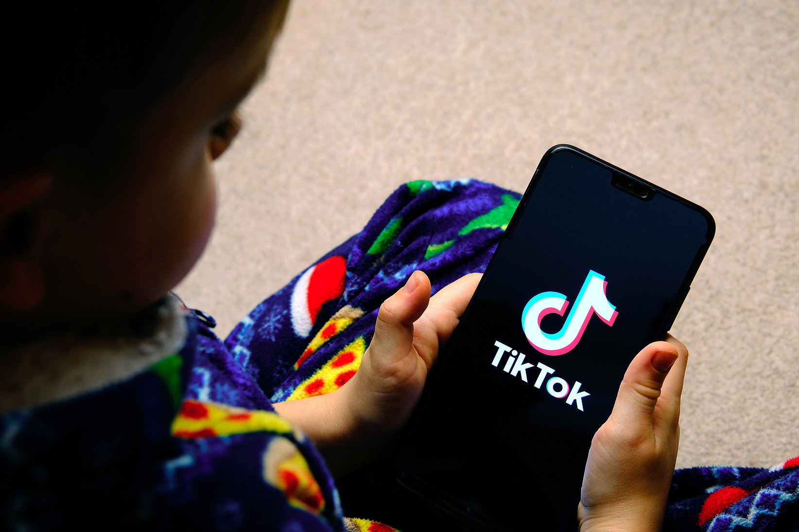A mobile phone is held in the hand of a little boy, where "TikTok" can be seen on the screenshot.