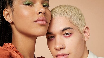 Genderless Beauty: cómo la Gen Z rompe con las normas de género Primer plano de dos personas maquilladas: una con sombra de ojos verde y la otra con el pelo decolorado y un aro en la nariz. Ambos modelos desprenden confianza con expresiones neutras.