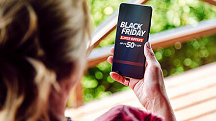 TikTok-Addicts unter sich Junge Frau hält ein Smartphone, das eine Black Friday Ad zeigt.