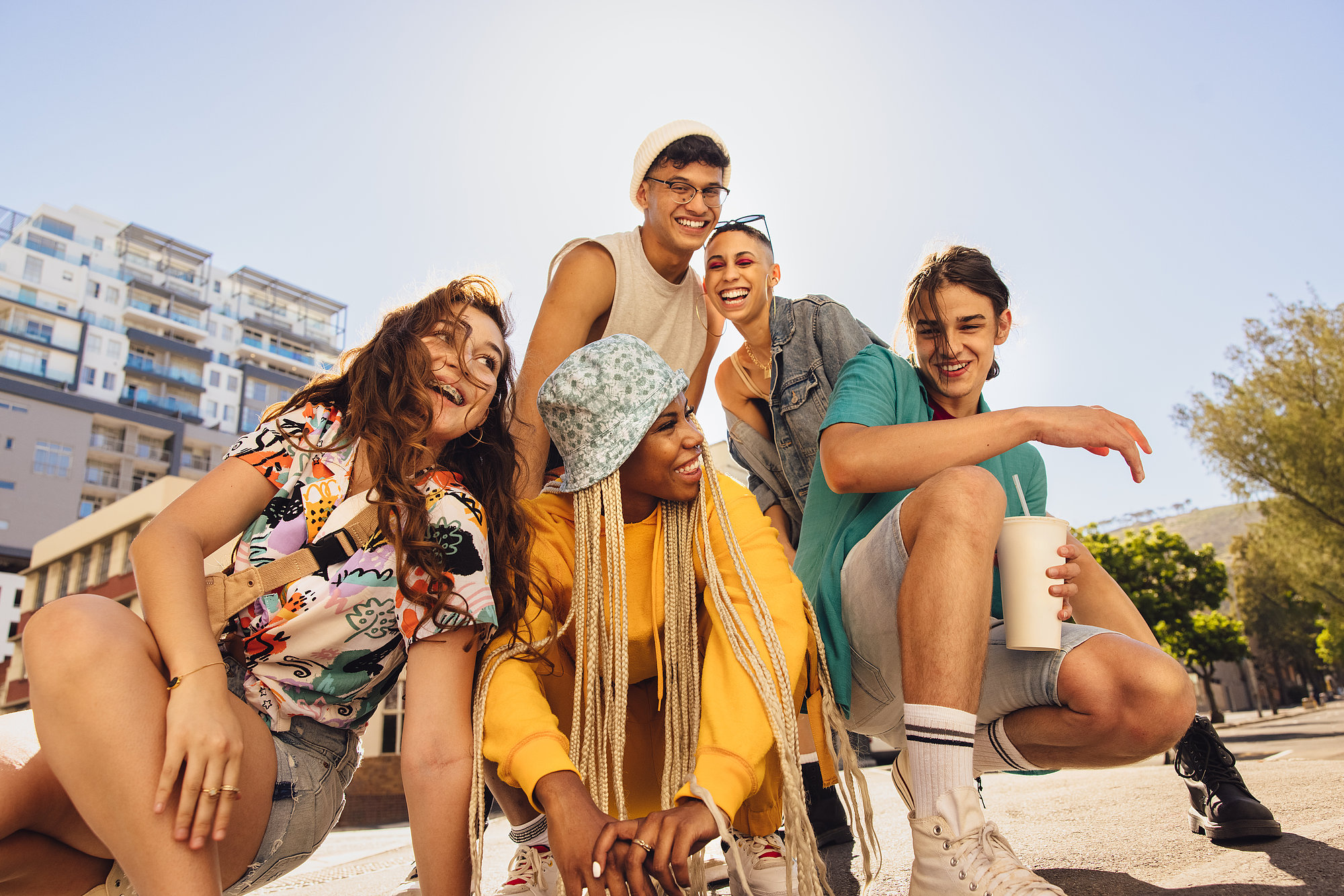 Un grupo de amigos jóvenes disfruta al aire libre, vestidos con ropa colorida y relajados, transmitiendo energía, diversión y camaradería en un día soleado.