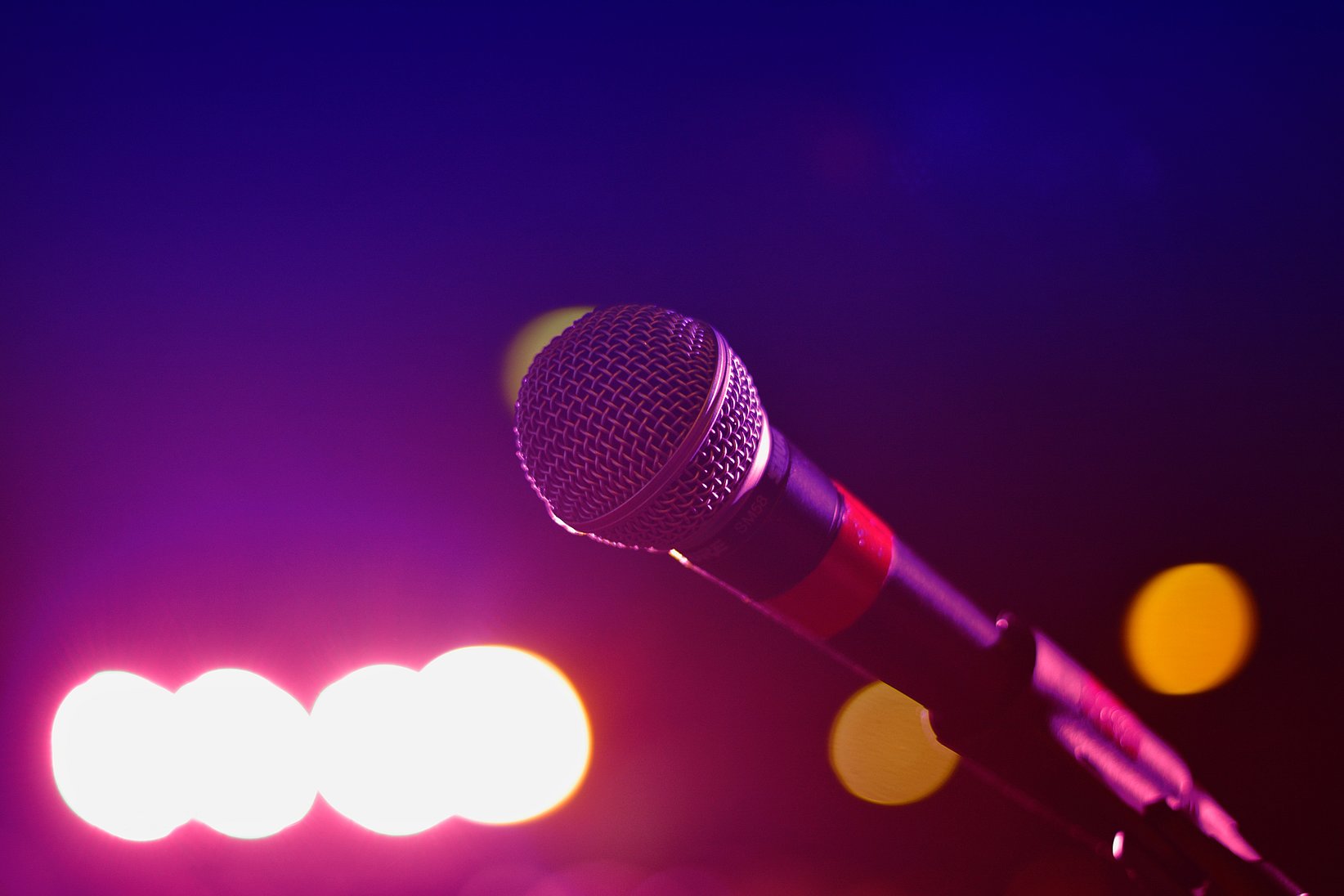 A microphone in the foreground, while it is dark but colourful lights can be seen in the back.