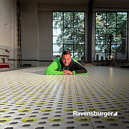 Mann in grüner Jacke liegt auf dem Boden und hat die Arme vorne zusammen. Er schaut frontal in die Kamera.