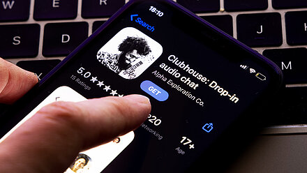 The Clubhouse Candle The screen of a mobile phone shows the Clubhouse app in the Appstore and that it is being downloaded.