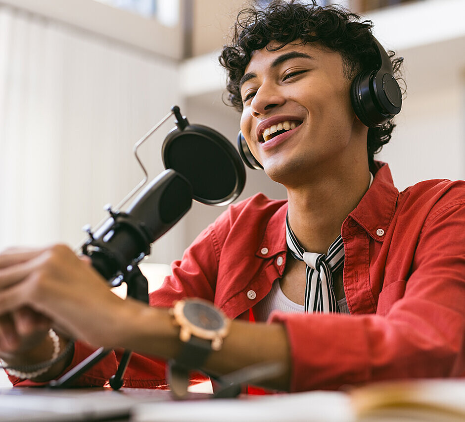 Junger Mann mit dunklen lockigen Haaren sitzt lächelnd vor einem Mikrofon