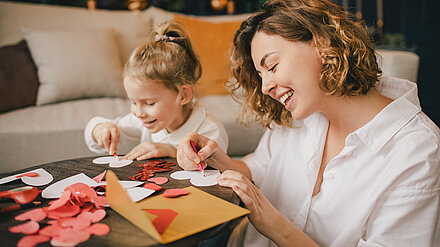 12 Things to do With Your Kids This Valentine's Day Mother and daughter happily tinker together at a table with colorful paper hearts and decorations.