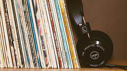 The Future of Music Consumption A row of records standing close together on a shelf, with a pair of black headphones leaning next to them.