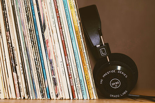 A row of records standing close together on a shelf, with a pair of black headphones leaning next to them. 