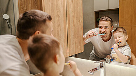 Gen Alpha zwischen Badespaß und Bürstenkämpfen Vater und Sohn putzen gemeinsam vor dem Badezimmerspiegel ihre Zähne.