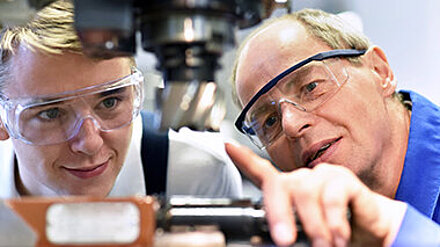 How to: Azubimarketing Ausbilder zeigt einem Azubi einen Vorgang an einer industriellen Maschine.